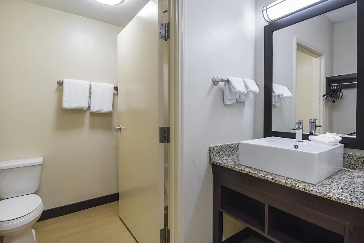 A bathroom with a white toilet, a sink with a granite countertop, and a mirror with a black frame.
