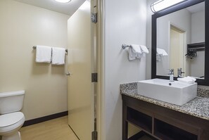 A bathroom with a white toilet, a sink with a granite countertop, and a mirror with a black frame.