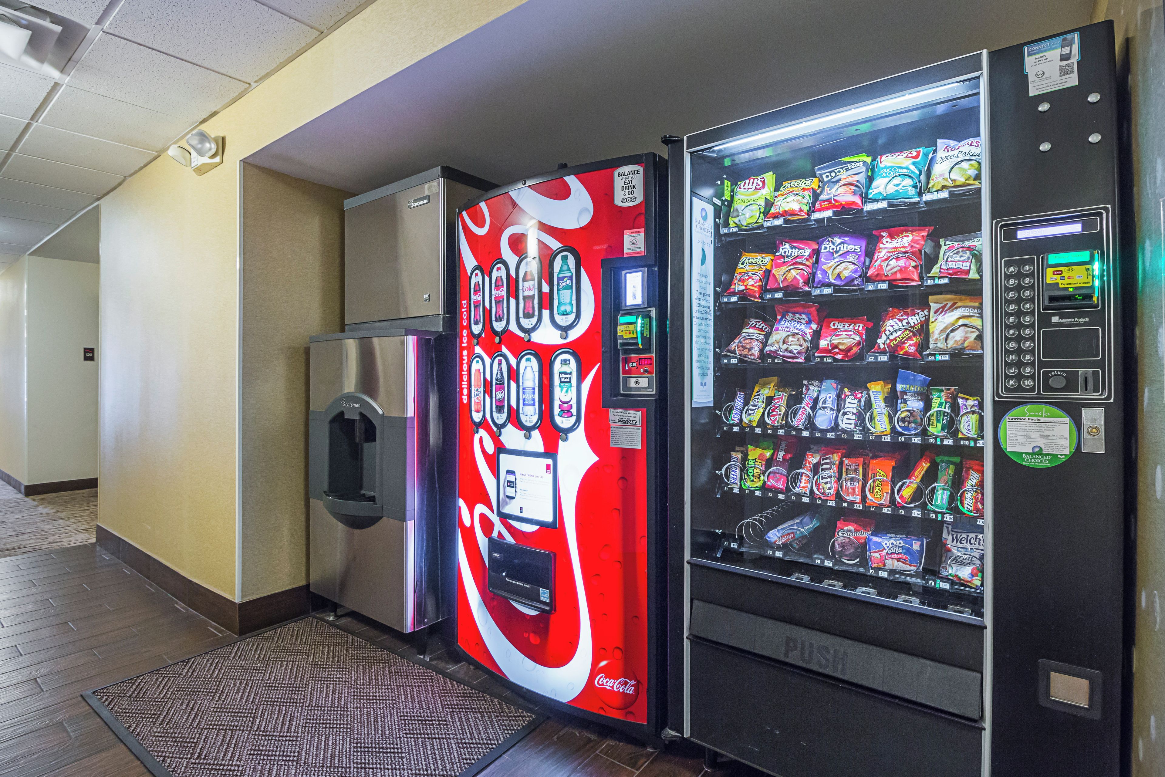 A vending machine and a refrigerator in a hallway.