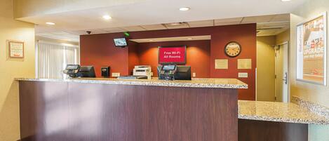A hotel reception desk with a digital screen, a clock, and a sign offering free Wi-Fi.