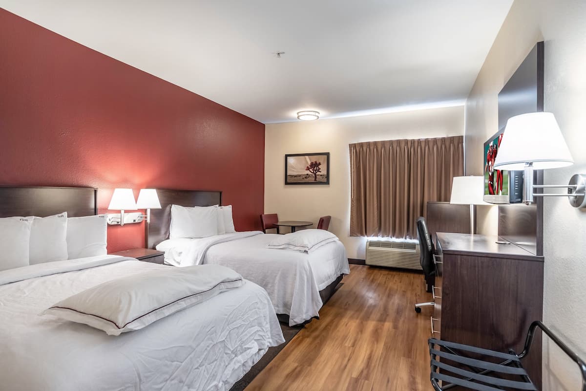 A hotel room with two beds, a desk, a chair, a lamp, and a picture on the wall.