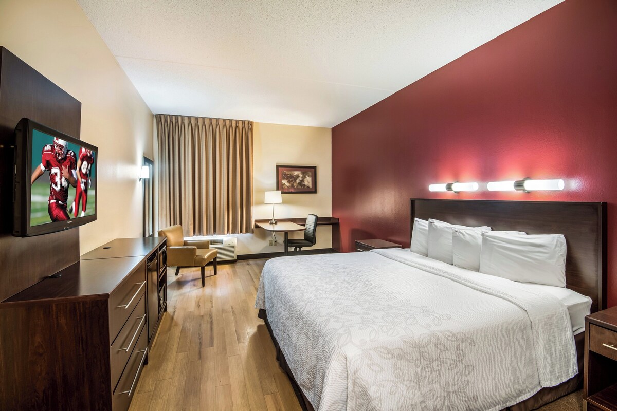 A hotel room with a bed, a desk, a chair, a TV, and a lamp.
