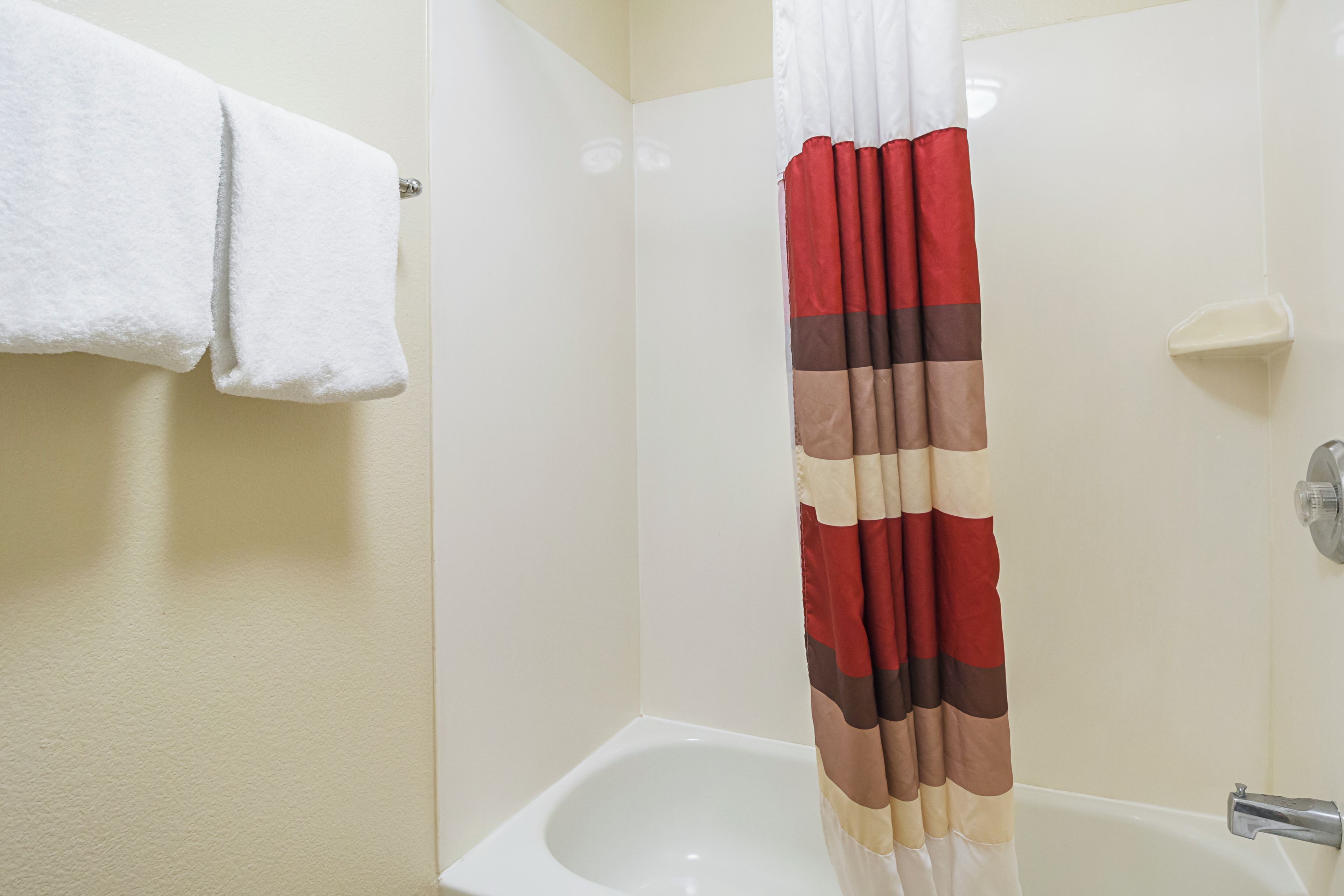 Een badkamer met een witte badkuip, een witte handdoek aan een rek en een douchegordijn in rood en beige.