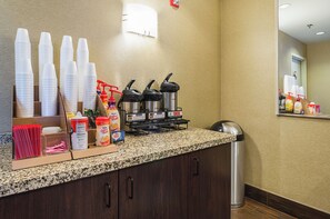 Una estación autoservicio para bebidas con vasos desechables, máquinas de café y dispensador de agua.