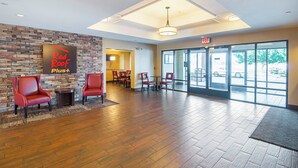 A lobby with a stone wall, red chairs, a reception desk, and a view of the parking area through large glass doors. - Red Roof Inn PLUS+ Phoenix West (Phoenix)