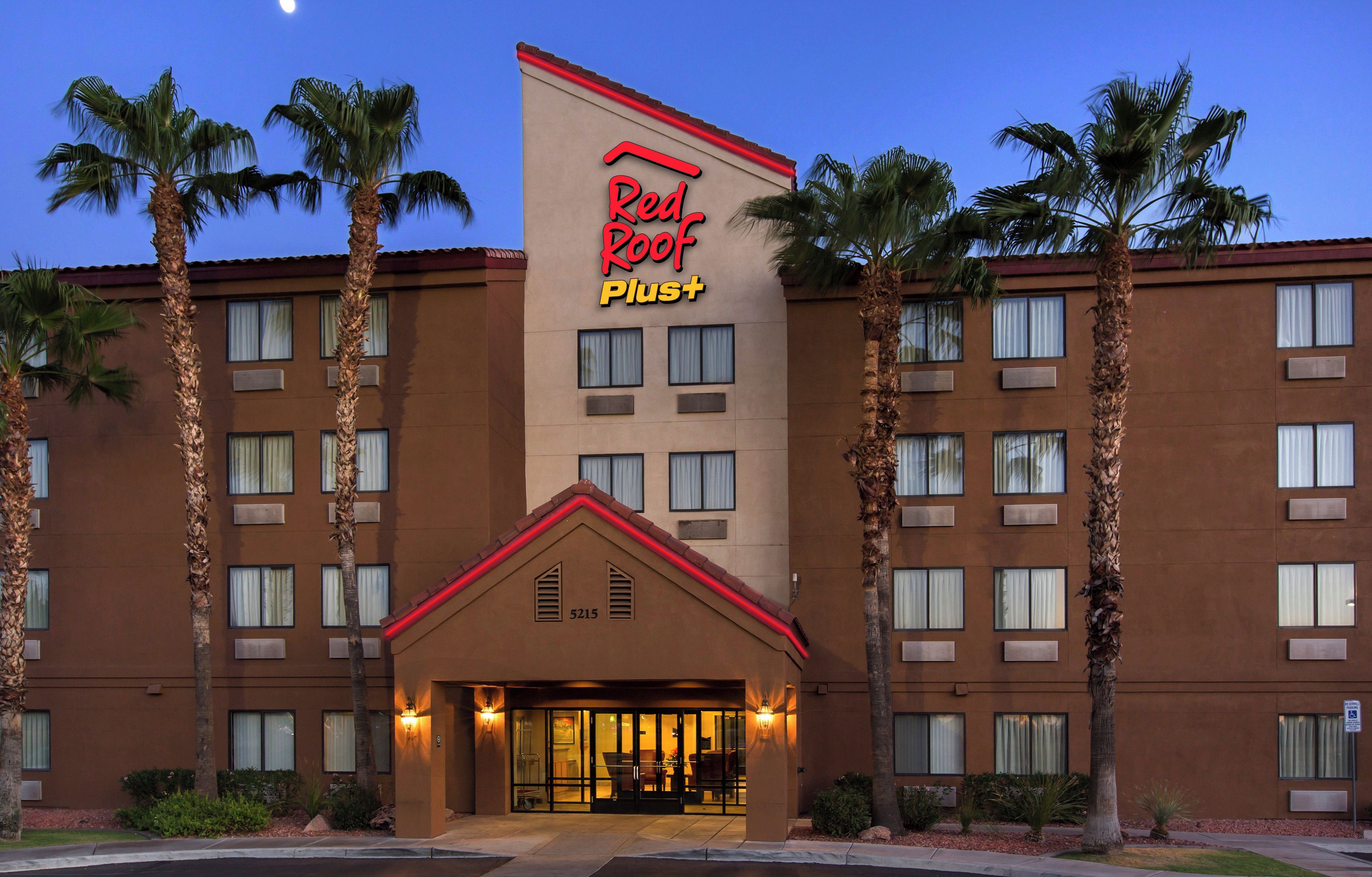 A hotel with a prominent Red Roof Plus sign, multiple floors, and a central entrance with a covered area.