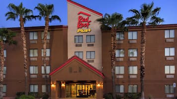 A hotel with a prominent Red Roof Plus sign, multiple floors, and a central entrance with a covered area.
