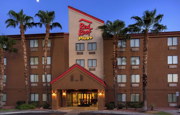 A hotel with a prominent Red Roof Plus sign, multiple floors, and a central entrance with a covered area.