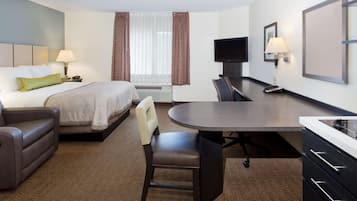 A hotel room with a bed, a desk, a chair, a TV, and a lamp.