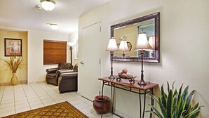 A hallway with a patterned rug, a console table with lamps, a potted plant, and a mirror on the wall. - Sonesta Simply Suites Knoxville (Knoxville)