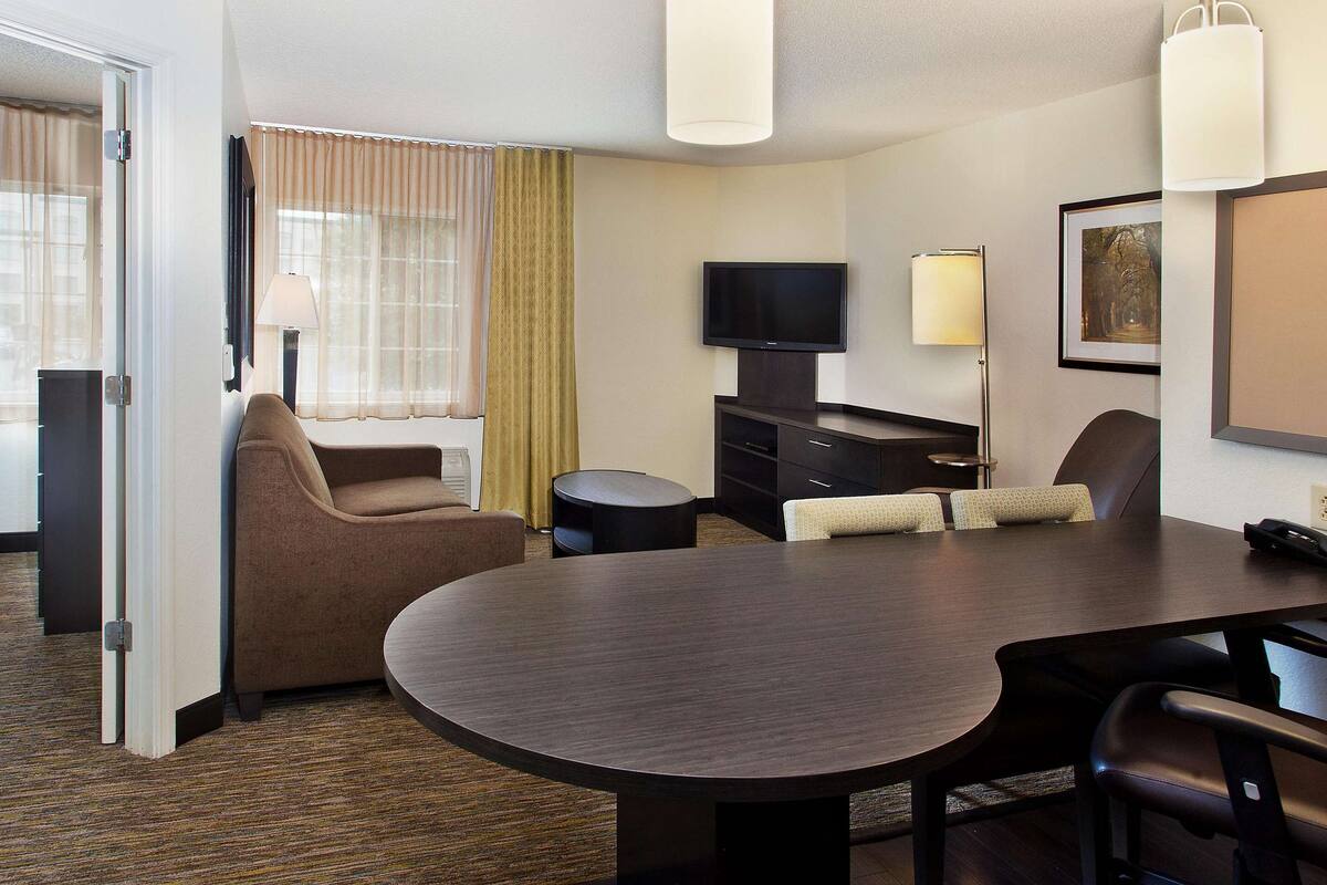 Una camera d'albergo con un letto, un'area salotto con tavolo e sedie, una televisione e una lampada.