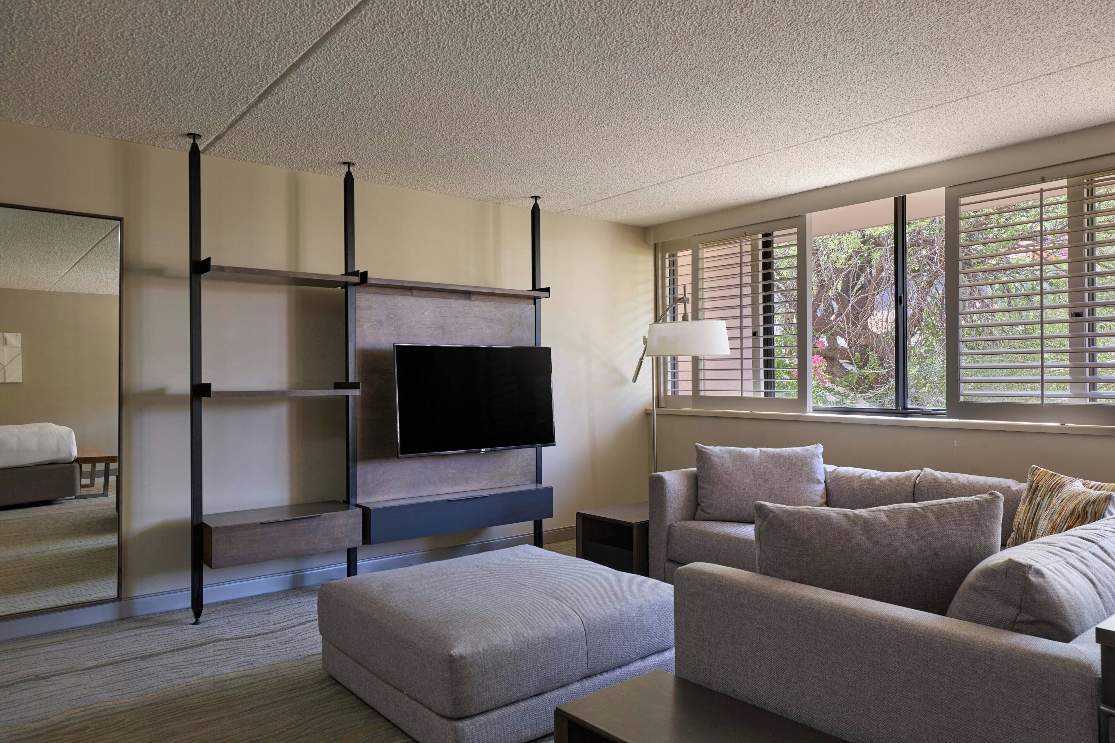 A modern living room with a flat-screen TV, a sofa, a coffee table, and a window with blinds.