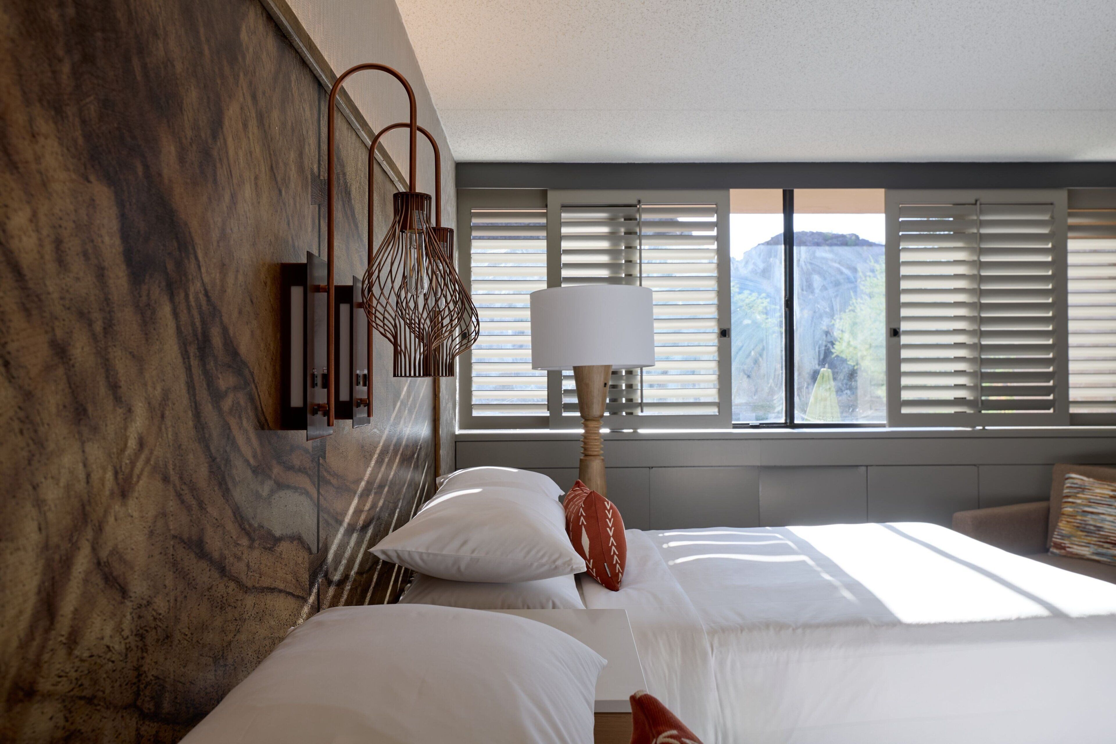 Ein Hotelzimmer mit Bett, Lampe und Bergblick durch das Fenster.