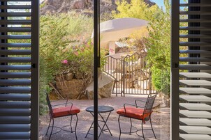 Un patio con dos sillas de metal y una mesa, con vistas a un jardín con rocas y plantas.