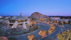 Un edifici modern amb una estructura piramidal única, una gran formació rocosa i una carretera sinuosa amb arbres il·luminats.