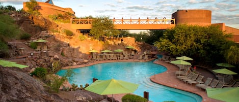 A pool area with lounge chairs and umbrellas, surrounded by rocks and vegetation.