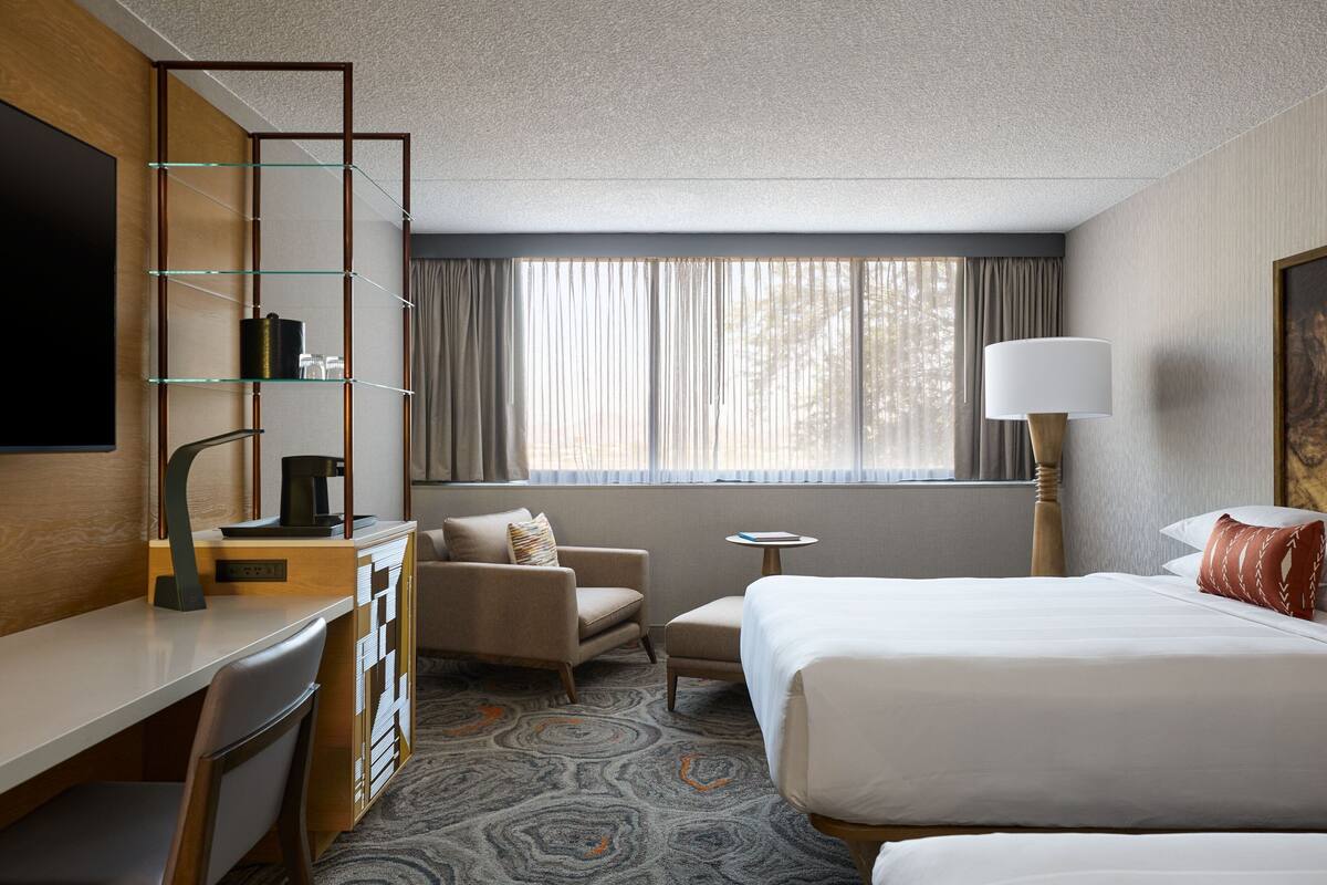 A hotel room with a bed, a desk, a chair, a small table, and a TV.