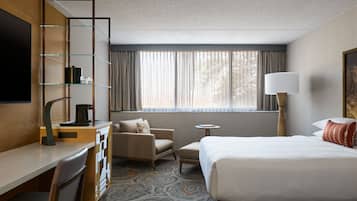 A hotel room with a bed, a desk, a chair, a small table, and a TV.