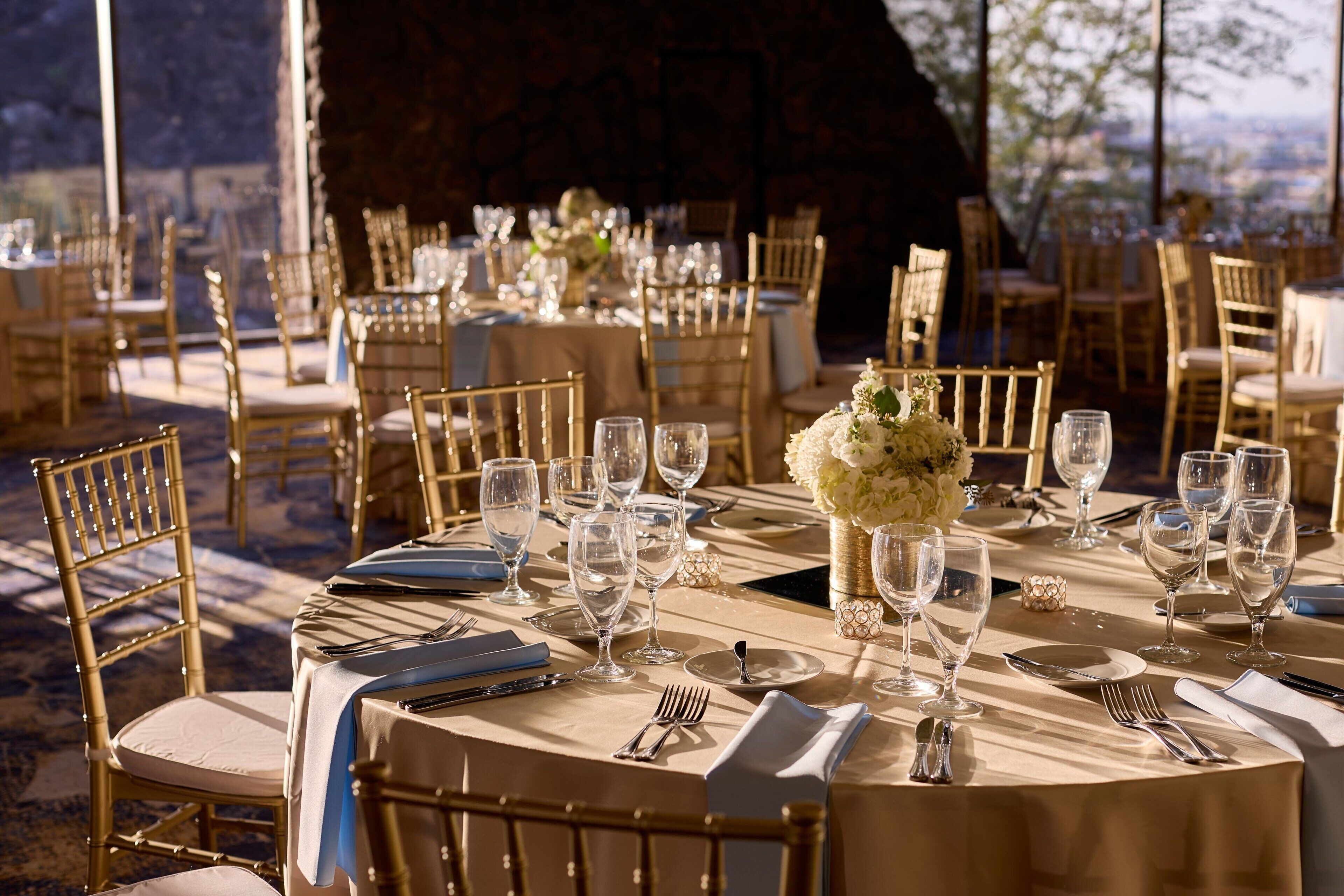 A well-set dining area with round tables, gold chairs, and clear glassware.
