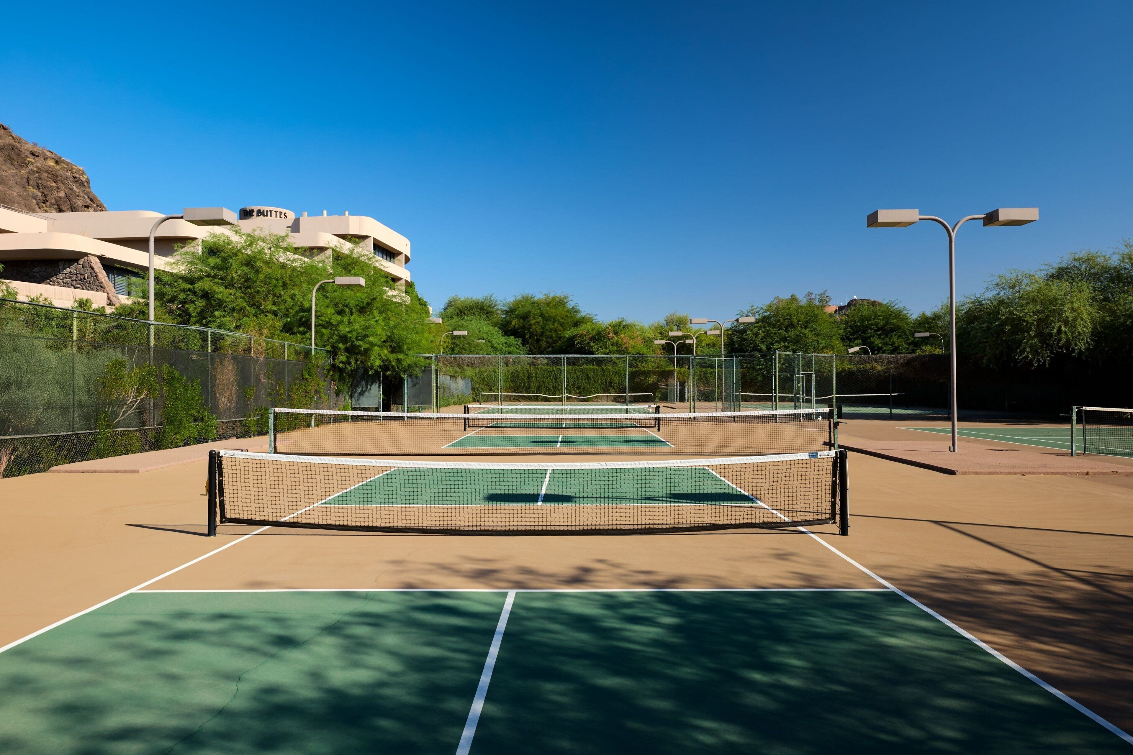 A tennis court with a net, surrounded by a fence and trees.