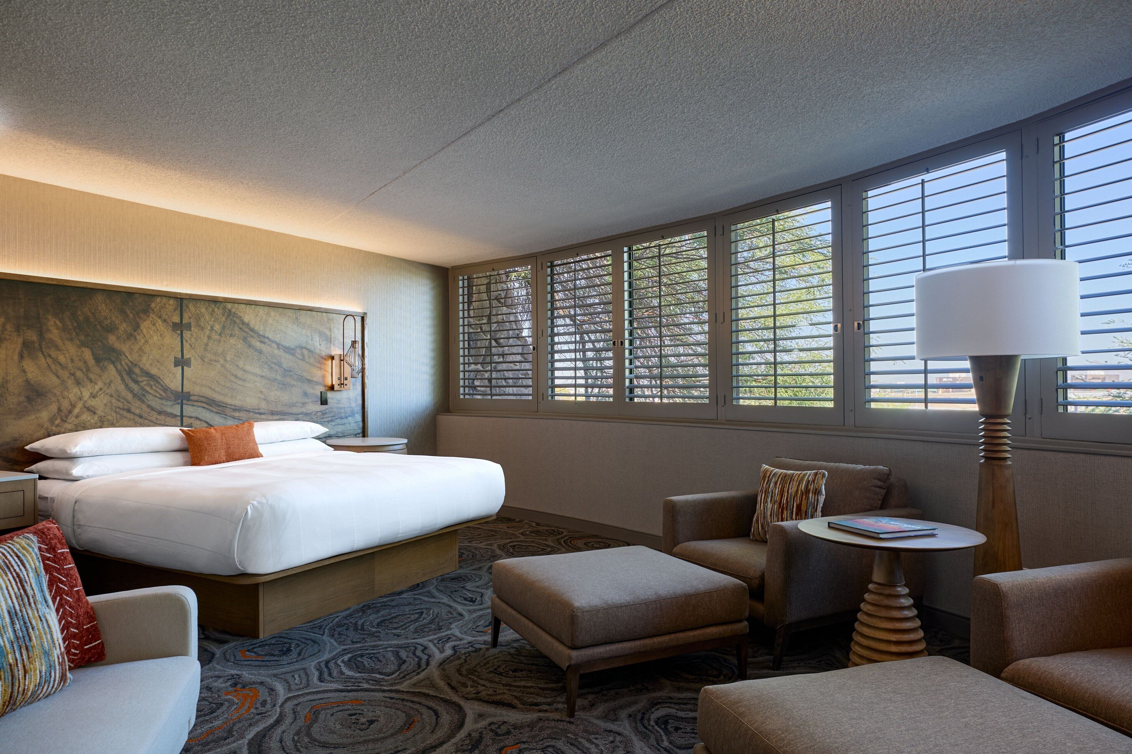 Une chambre d’hôtel avec un grand lit, un canapé, un pouf, une petite table et une lampe.