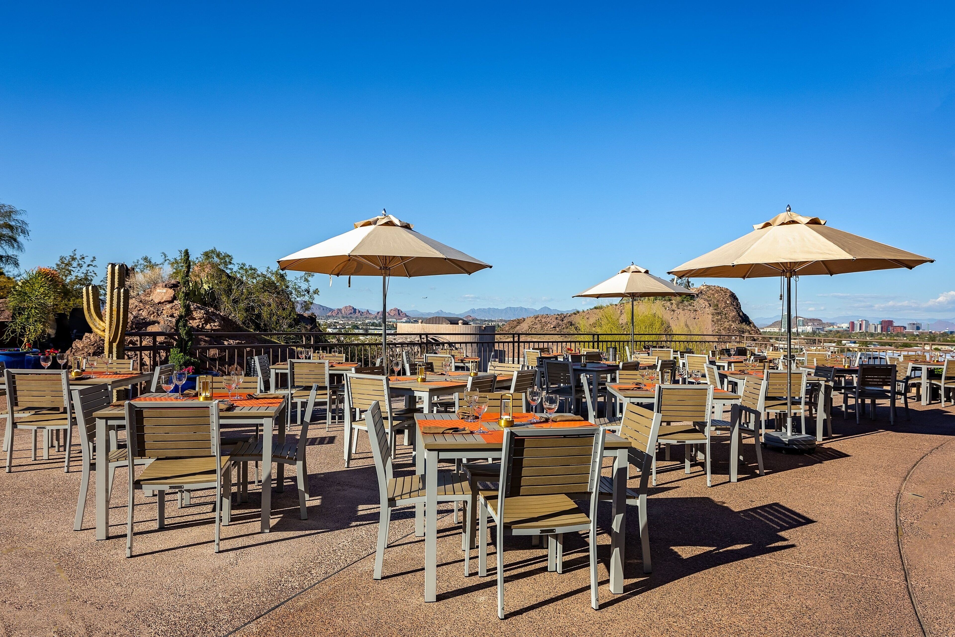 Outdoor seating with tables and chairs, umbrellas, and a desert landscape in the background.