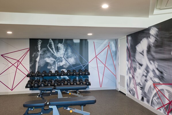 A gym with a bench press, dumbbells, and a wall with geometric patterns.