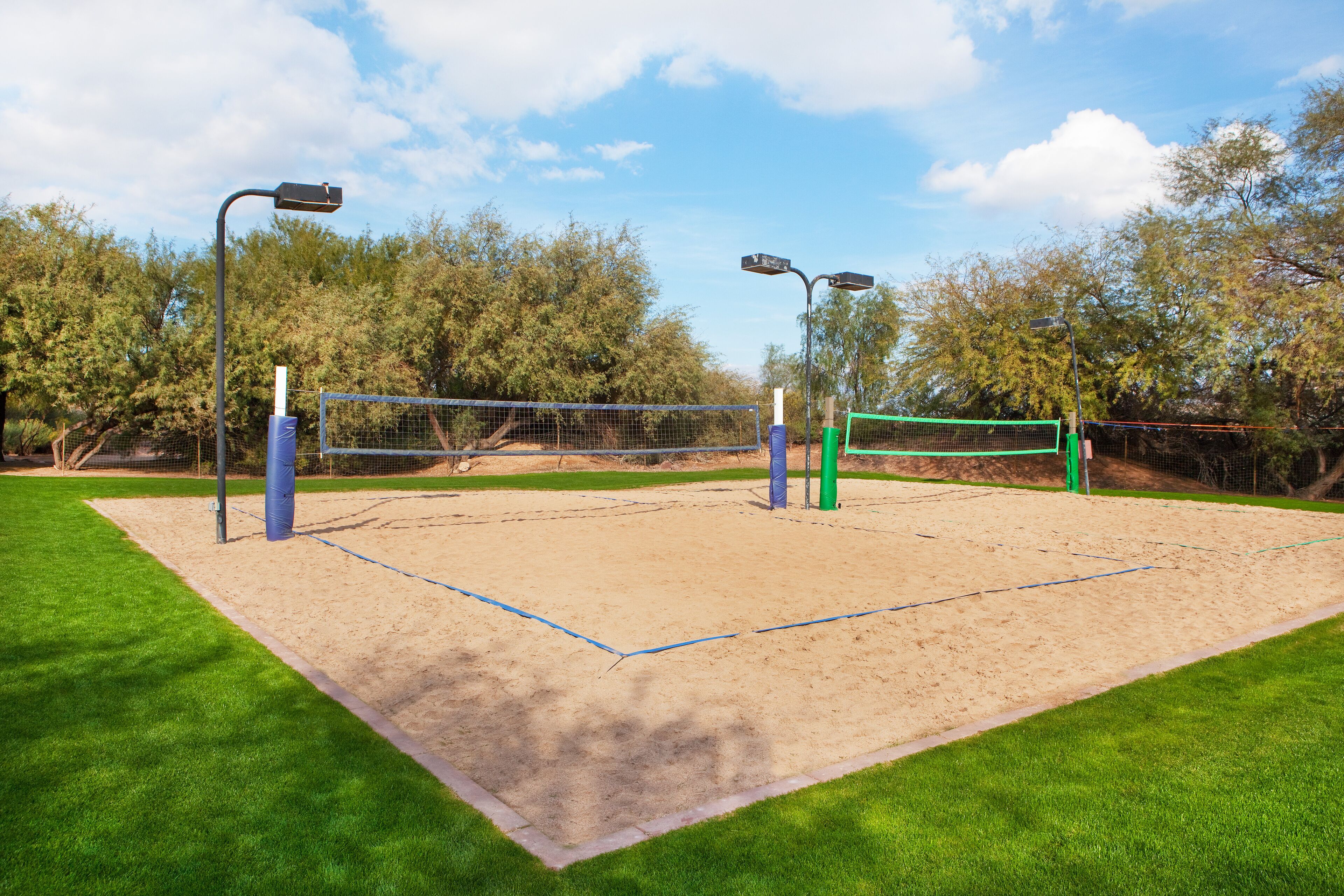 A sand volleyball court with net, surrounded by green grass and trees.