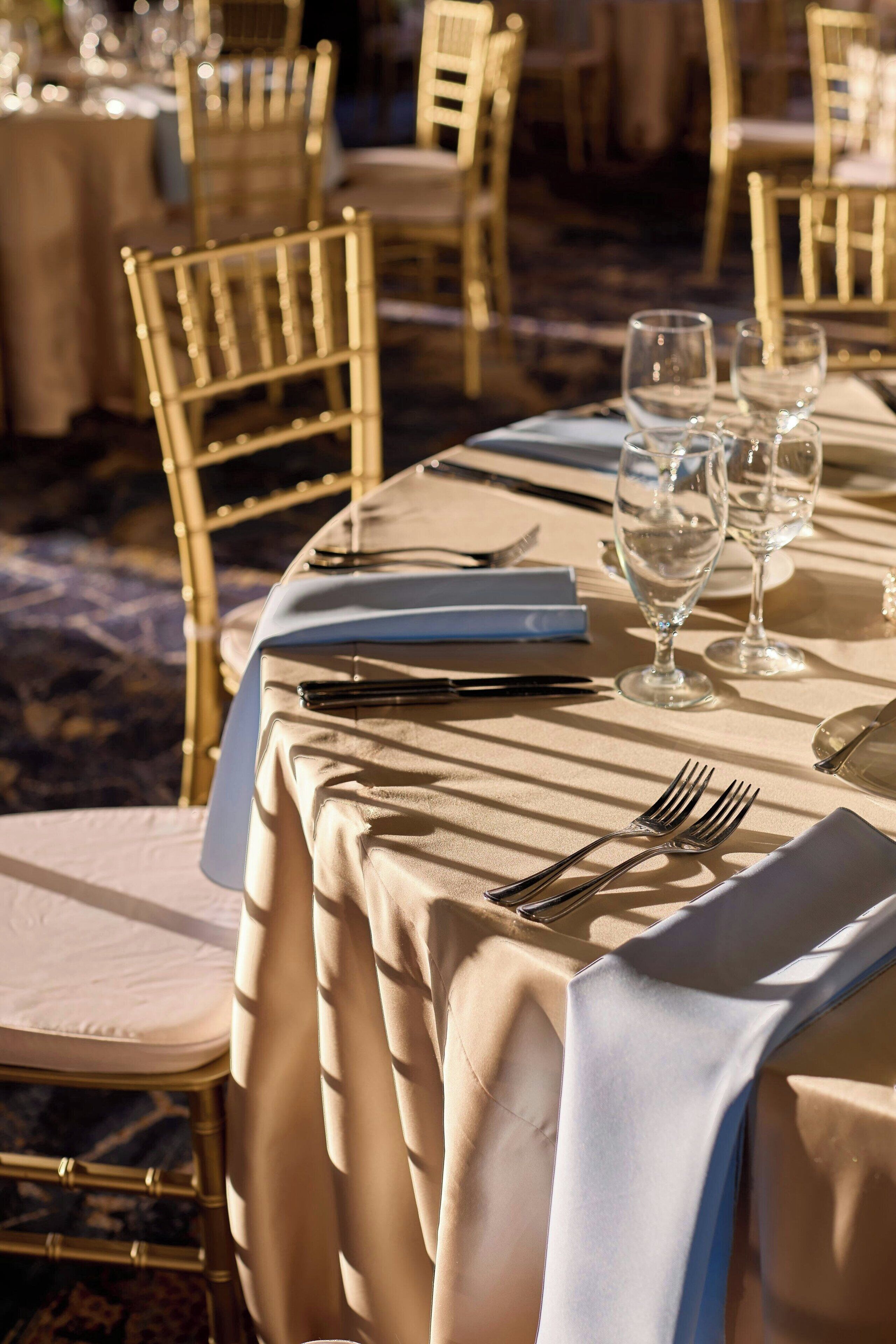A dining table set with a white tablecloth, gold chairs, and empty wine glasses.