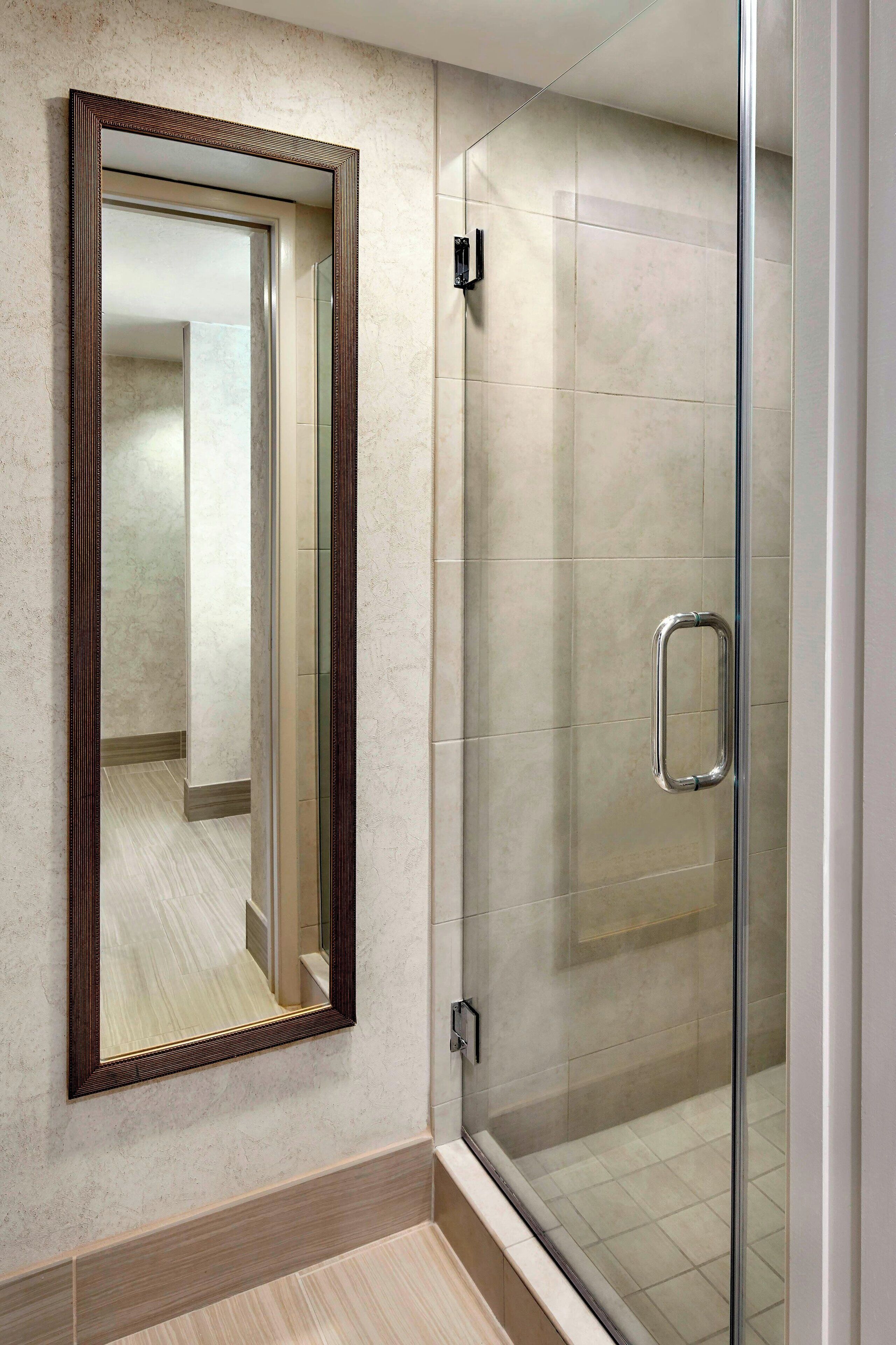 A bathroom with a glass-enclosed shower, a large mirror, and a tiled floor.