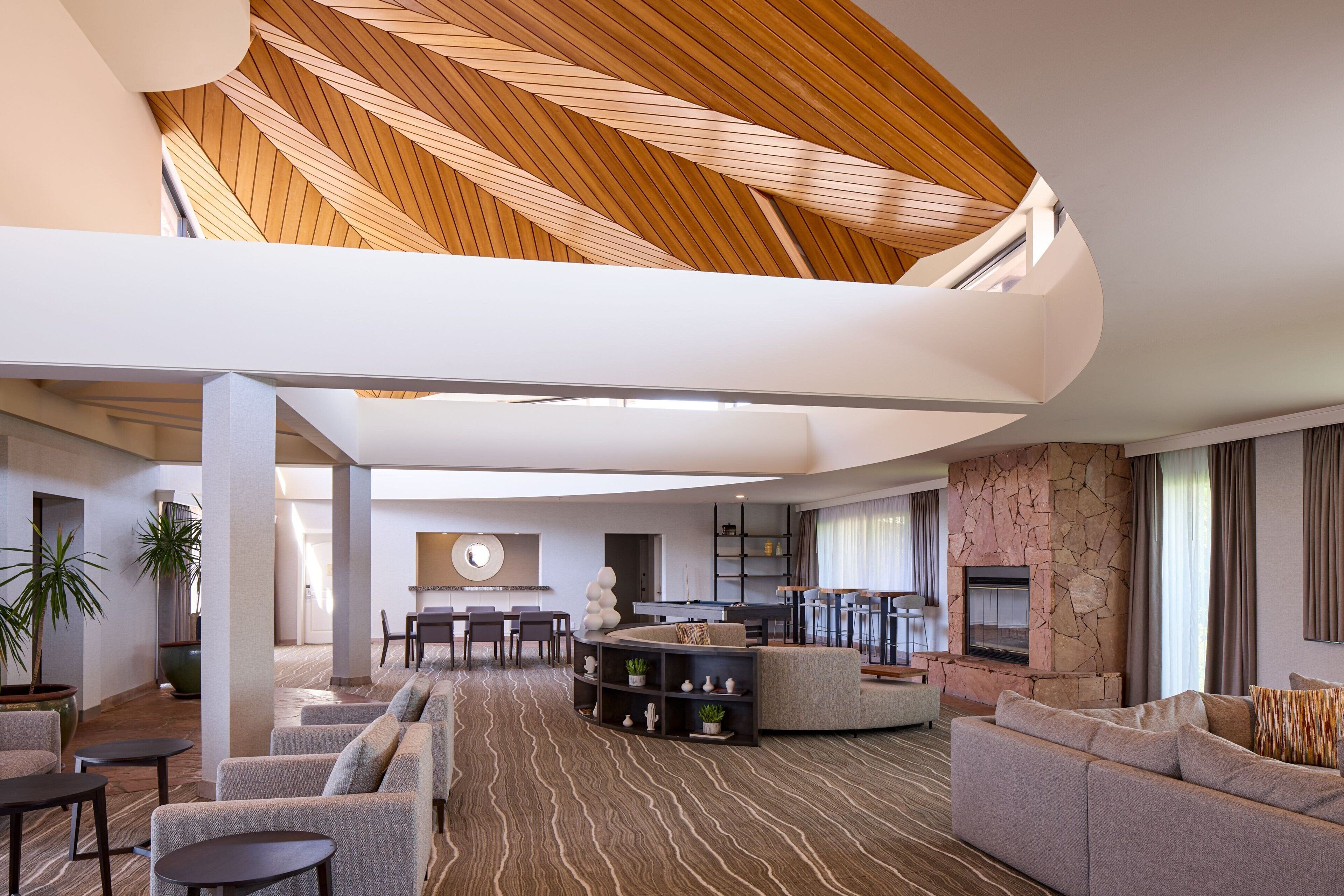 A spacious living area with a curved ceiling, a stone fireplace, and a modern kitchen in the background.