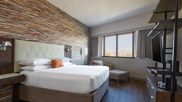 Une chambre d’hôtel moderne dotée d’un grand lit, d’un téléviseur à écran plat, d’un bureau intégré et offrant une vue sur les montagnes par la fenêtre.