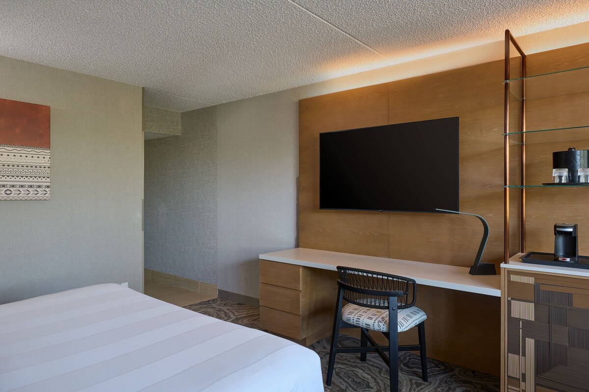 A hotel room with a bed, a desk with a chair, a flat-screen TV, and a coffee maker.