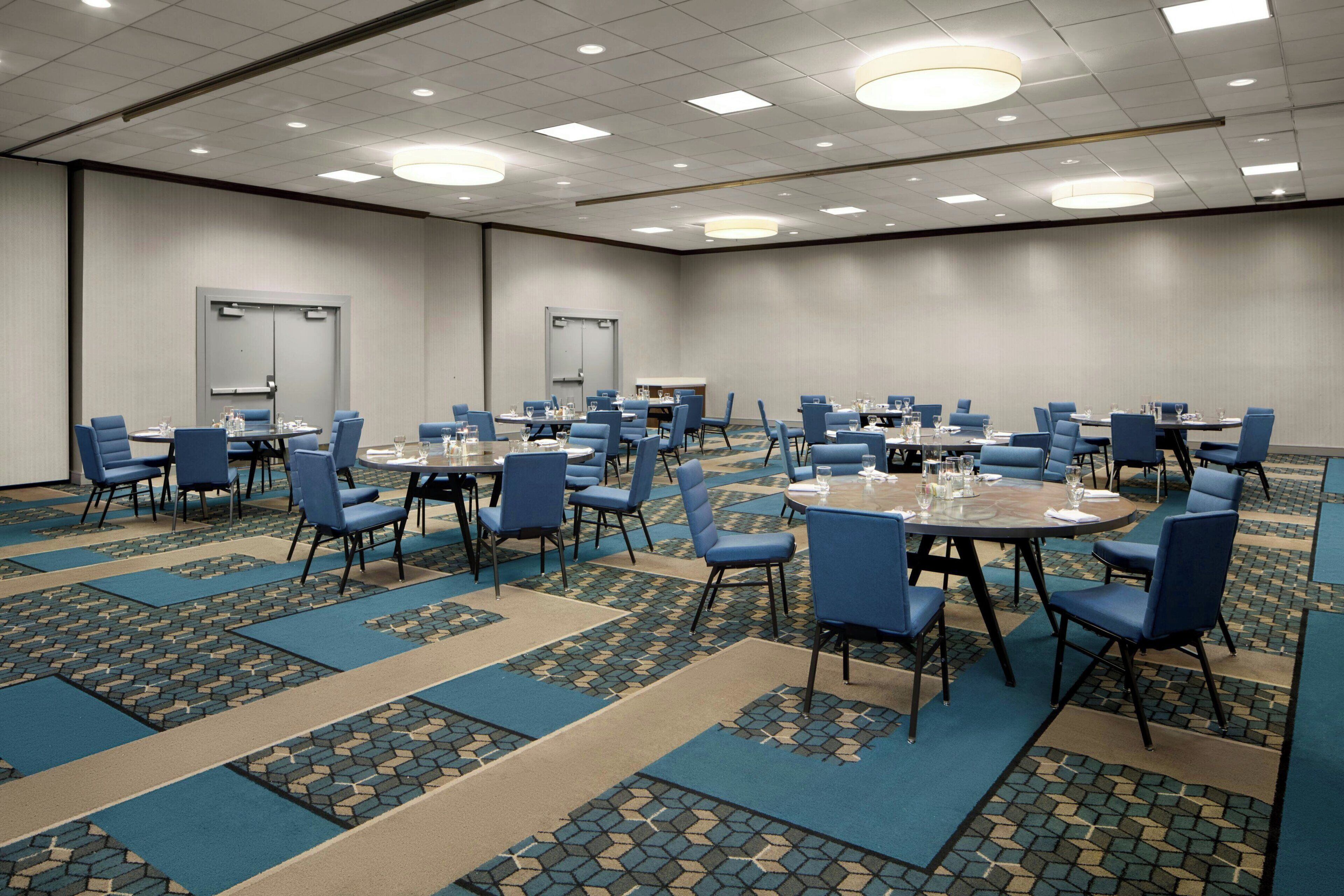 A large conference room with multiple tables and chairs, carpeted floors, and recessed lighting.