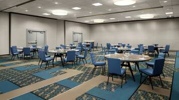 A large conference room with multiple tables and chairs, carpeted floors, and recessed lighting.