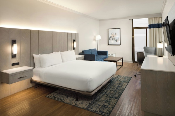 Una habitación de hotel moderna con una cama grande, mesitas de noche, un escritorio, una silla, un televisor y una ventana con cortinas.