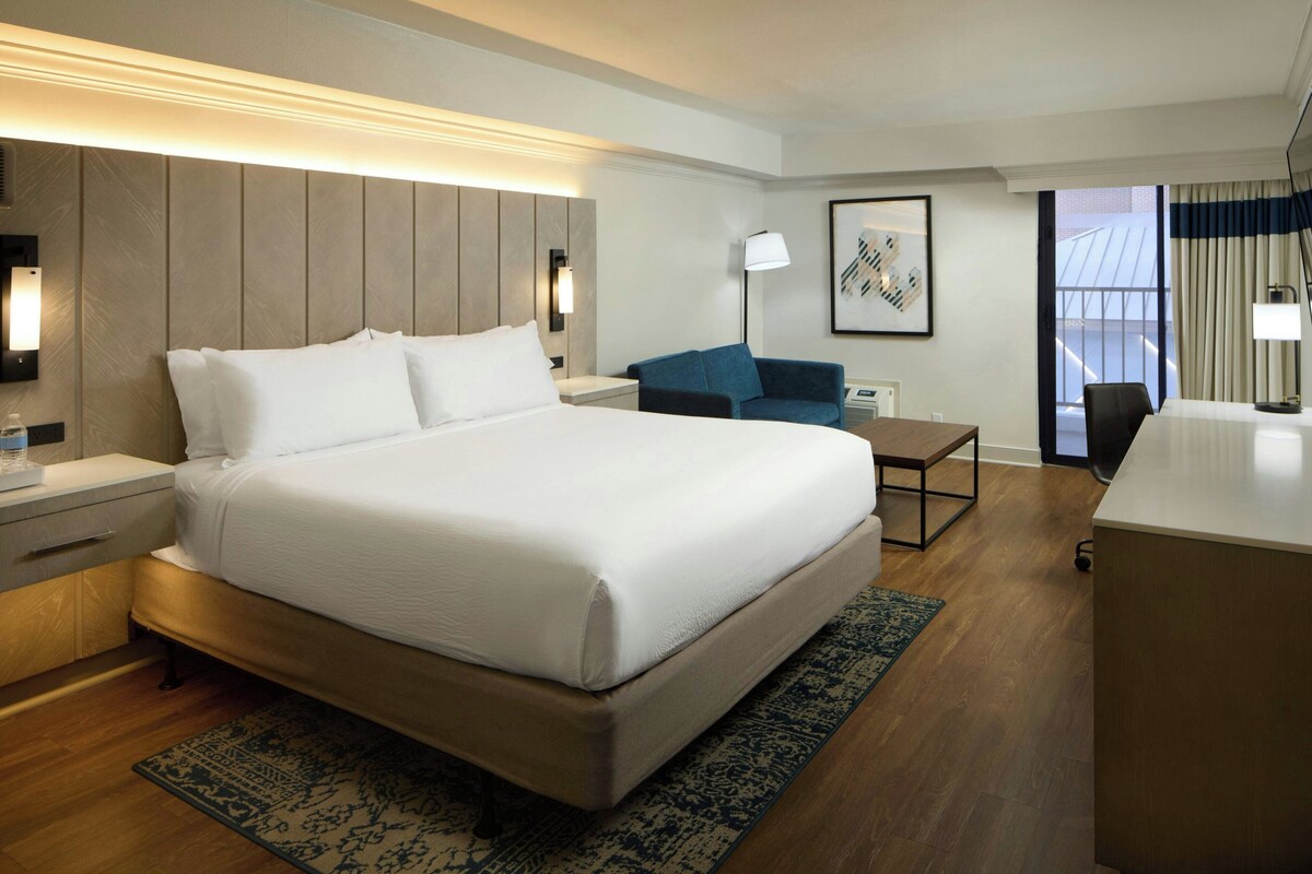 Een hotelkamer met een groot bed, een bureau, een stoel, een klein tafeltje en een bank.