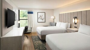 Habitación de hotel con dos camas, un escritorio, un televisor de pantalla plana, una lámpara y una ventana con cortinas.