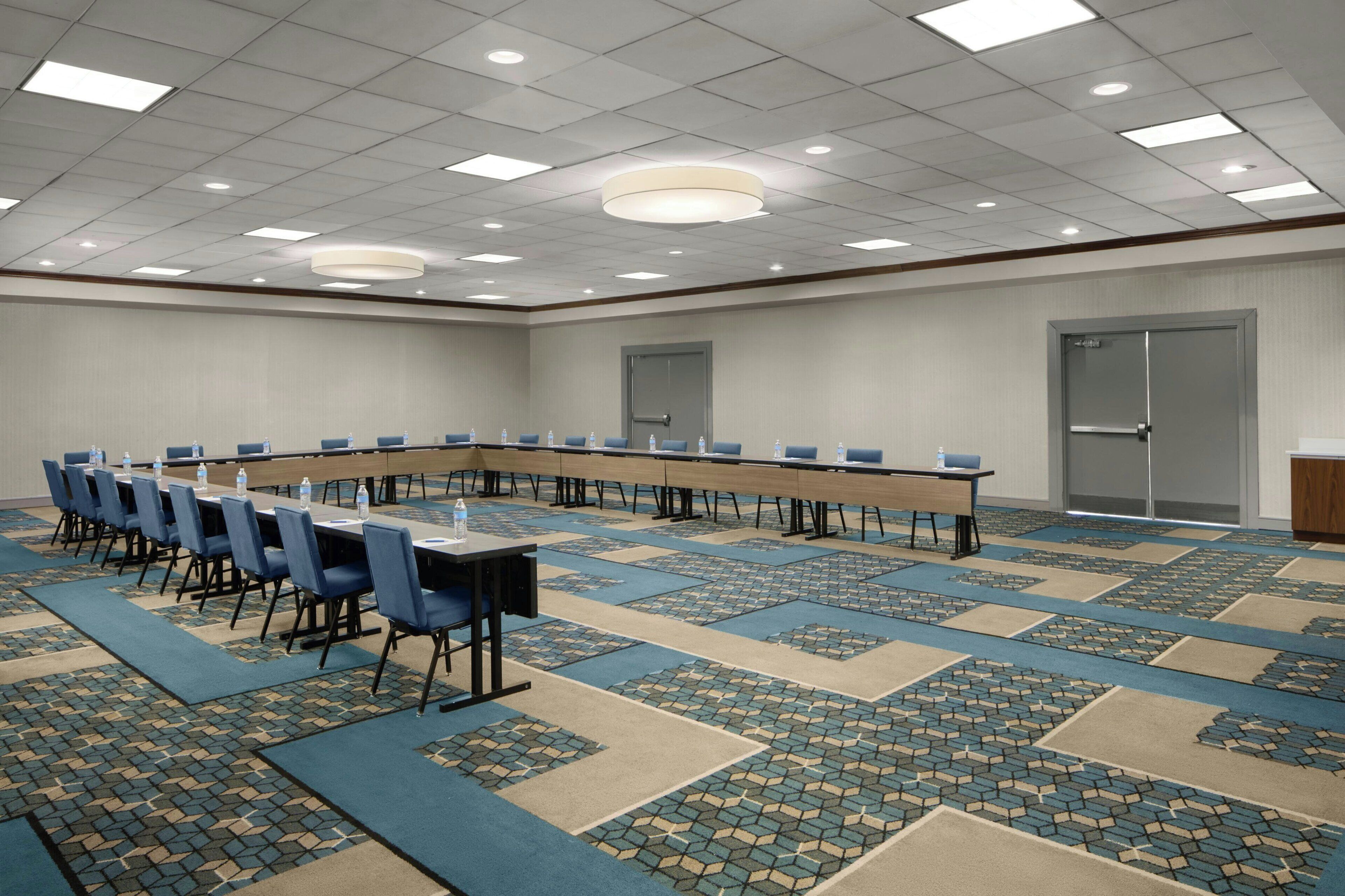 Un salón de conferencias con una larga mesa, sillas azules y una alfombra estampada.