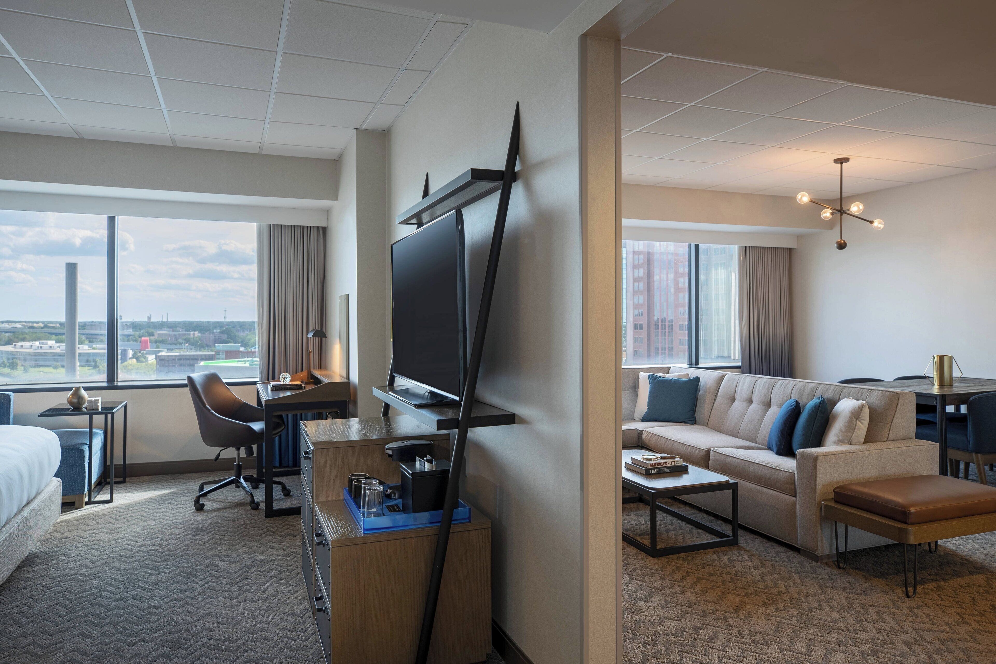 A hotel room with a large bed, a desk with a TV, a sofa, and a view of the city.