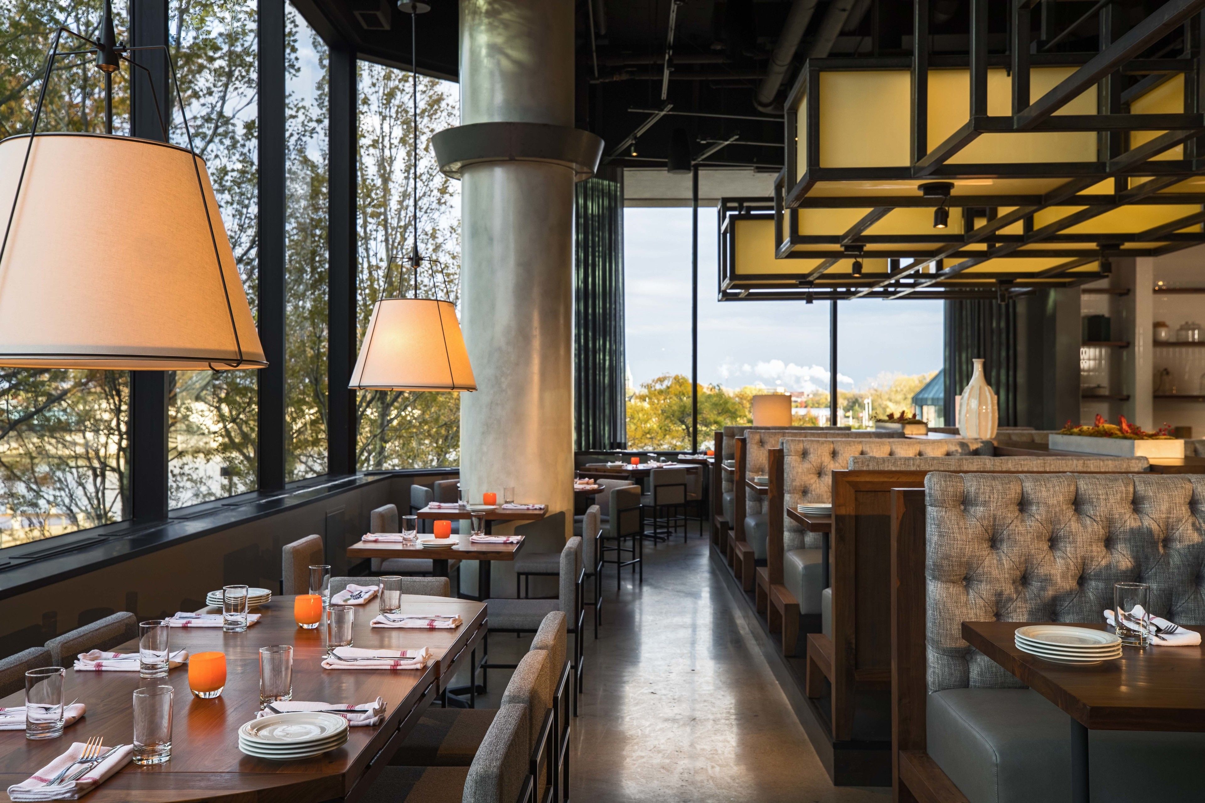 Un restaurante con mesas dispuestas para comer, grandes ventanales y vistas al exterior.