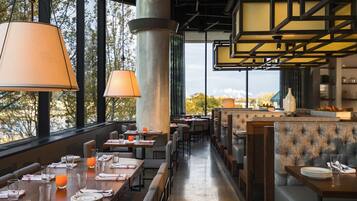 Un restaurante con mesas dispuestas para comer, grandes ventanales y vistas al exterior.