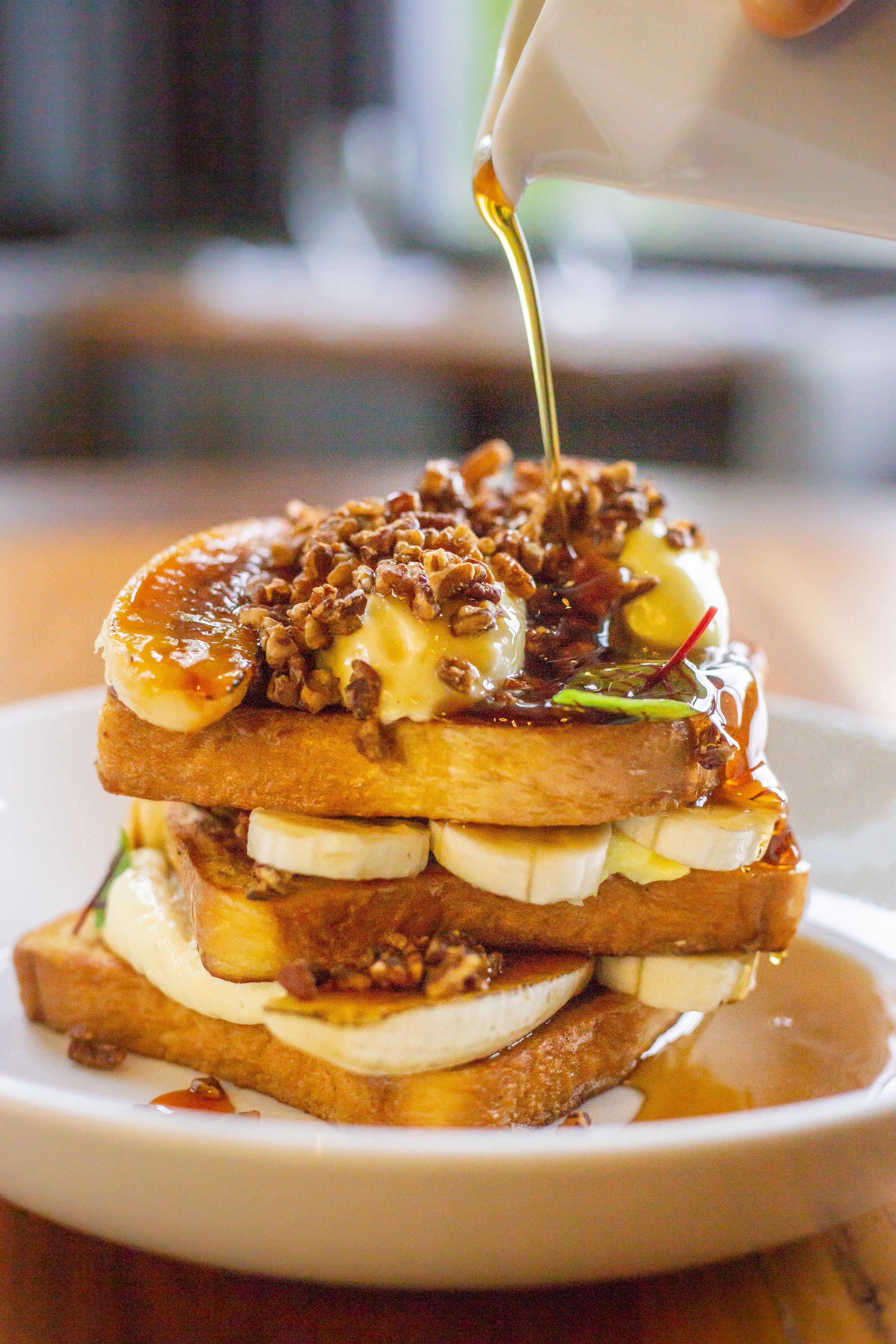 A stack of pancakes with bananas, nuts, and syrup.