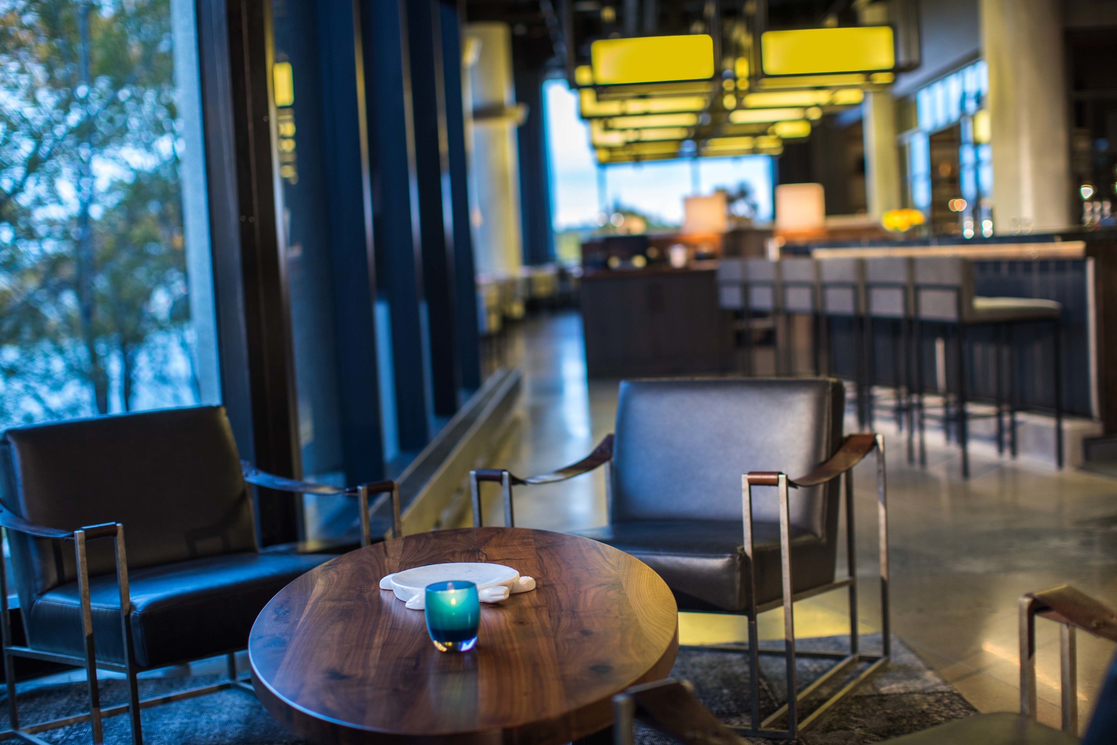 Un espace détente moderne avec une table ronde en bois, deux fauteuils en cuir et une bougie en verre bleue.