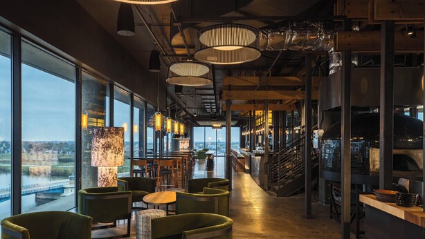 Ein modernes Interieur mit großen Fenstern, grünen Polstersesseln und einer Treppe, die zu einer oberen Ebene führt.