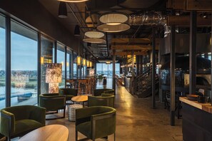 A modern interior with large windows, green upholstered chairs, and a staircase leading to an upper level.