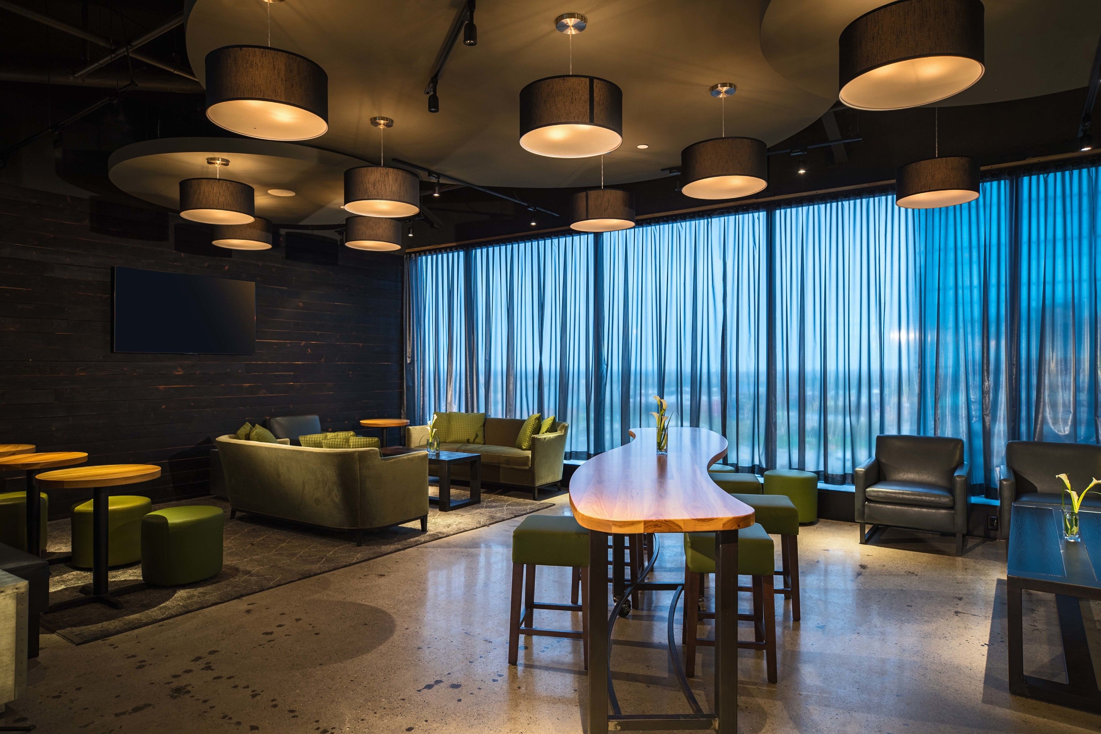 A modern lounge area with a wooden table, green ottomans, and leather chairs.