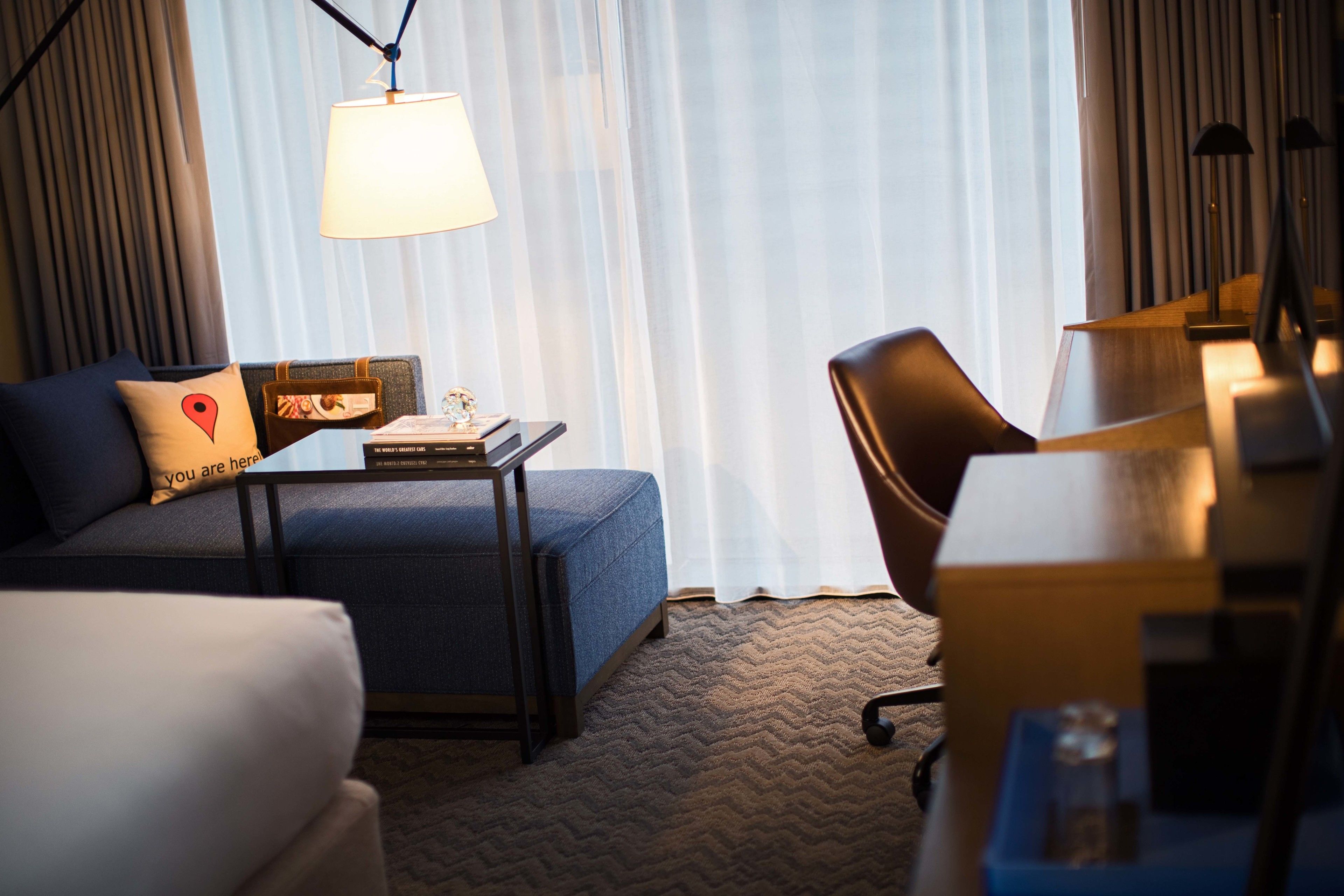 Een hotelkamer met een bank, een kleine tafel met een lamp, een bureau en een stoel.