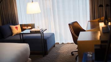 Een hotelkamer met een bank, een kleine tafel met een lamp, een bureau en een stoel.