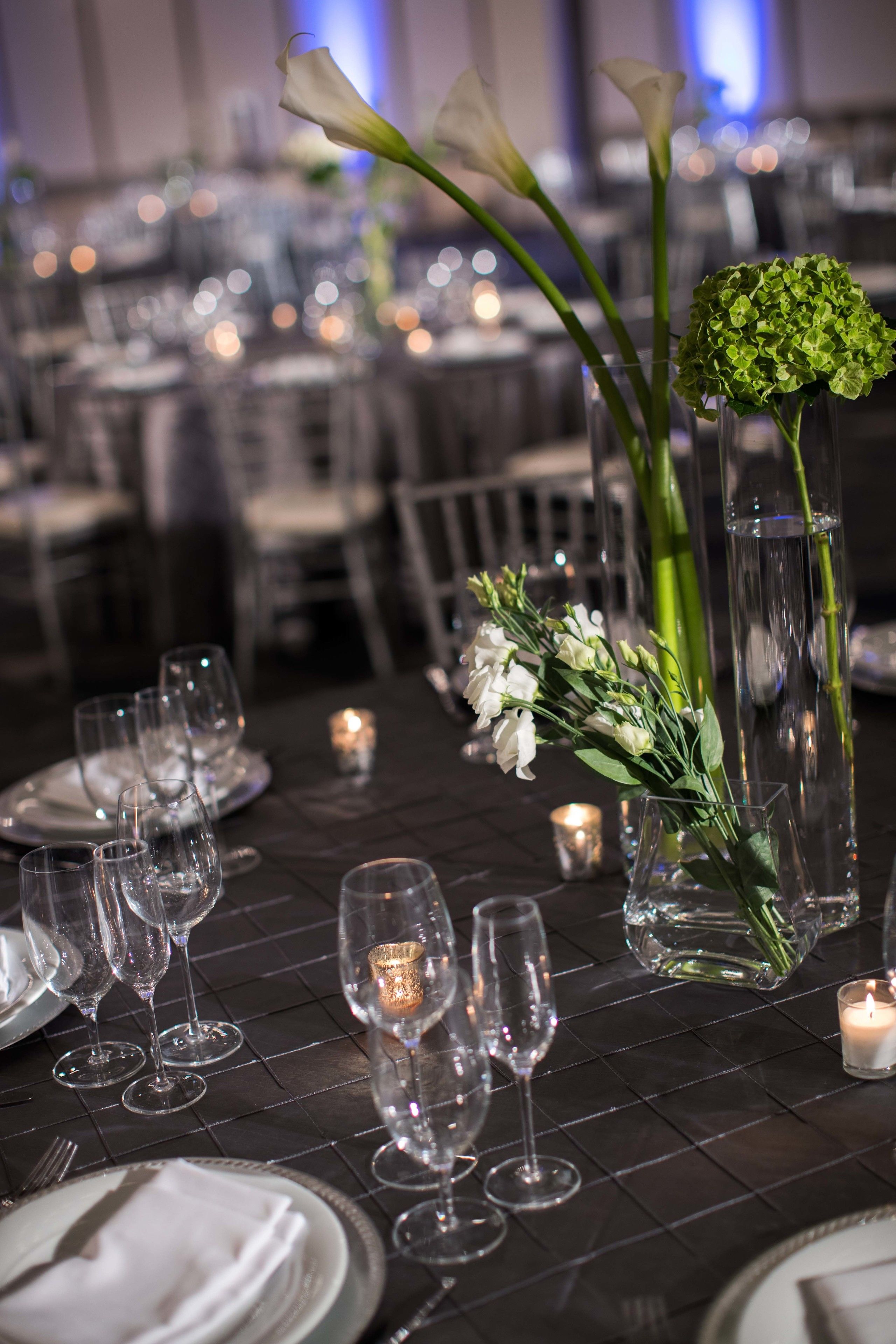 Una mesa dispuesta para un evento formal, con copas transparentes, platos blancos y centros de mesa florales.